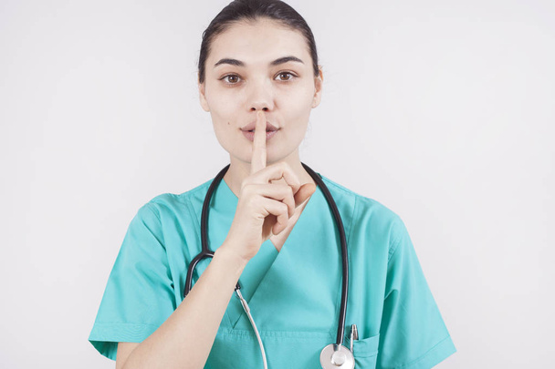 Νέοι νοσοκόμα γυναίκα πέρα από το απομονωμένο υπόβαθρο ζητώντας να είναι ήσυχη με το δάχτυλο στα χείλη. Σιωπή και μυστικό έννοια - Φωτογραφία, εικόνα