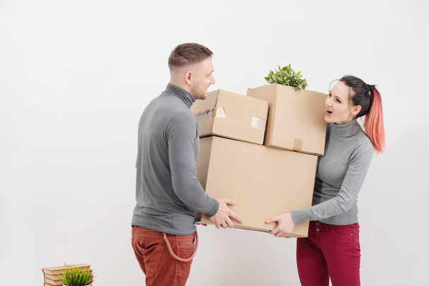 A young woman and a man carry heavy cardboard boxes with things. White light apartment. They laugh and kiss. - Foto, Bild