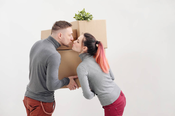 A young woman and a man carry heavy cardboard boxes with things. White light apartment. They laugh and kiss. - Foto, afbeelding