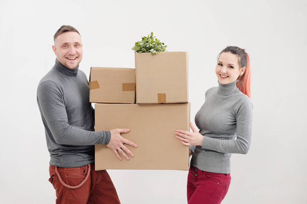Uma jovem e um homem carregam caixas de papelão pesadas com coisas. Apartamento de luz branca. Eles riem e beijam
. - Foto, Imagem