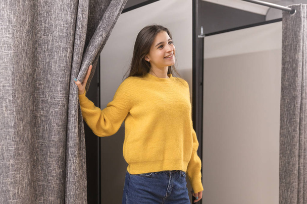 Jovencita en tienda de ropa probándose un suéter amarillo
 - Foto, Imagen