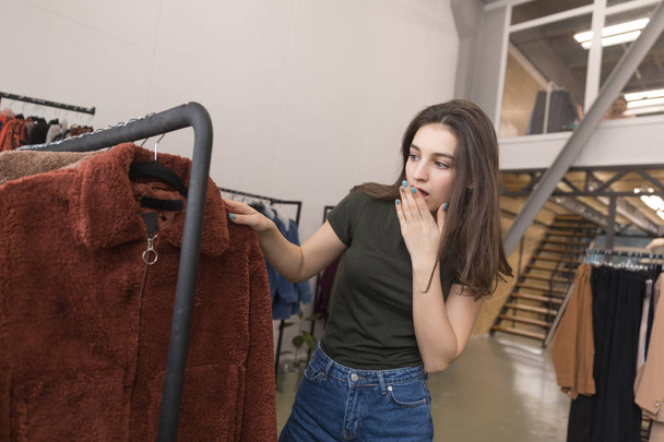 The girl in the clothing store chooses a new fur coat. - Foto, afbeelding