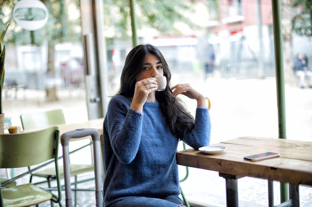 Красивая молодая женщина сидит за чашечкой кофе в кафе
 - Фото, изображение