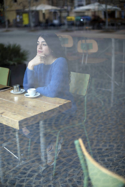 Portrait of a beautiful woman sitting in a cafe hand on chin while looking through glass pensive - Fotó, kép