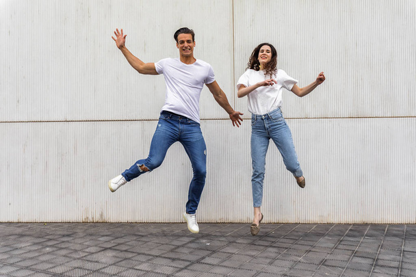 Happy couple in love jumping against grey wall. - Foto, Bild