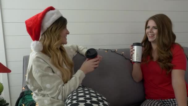 Two girls is sitting on sofa and drinking coffee at christmas time - Metraje, vídeo