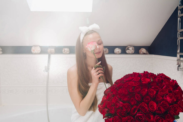 Ελκυστική γυναίκα σε πετσέτα και το στήριγμα κεφαλής με μπουκέτο από κόκκινα τριαντάφυλλα. - Φωτογραφία, εικόνα