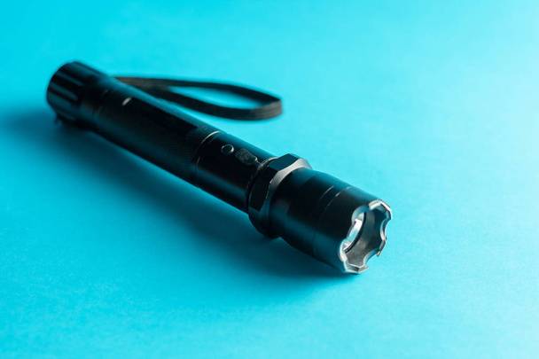 eine schwarze Metall-Taschenlampe mit Schocker auf blauem Hintergrund. pr - Foto, Bild