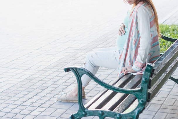 Pregnant woman is sitting on the bench in the park, soft focus background - Fotó, kép