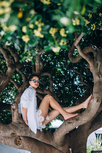 Güzel kadın bir ağaçta oturuyor. Bahar zamanı - Fotoğraf, Görsel