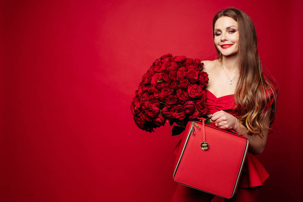 stilvolle hinreißende Brünette in Rot mit roten Rosen und roter Tasche. - Foto, Bild