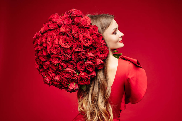 Beautiful young brunette lady in red with bunch of red roses on shoulder. - Foto, Bild
