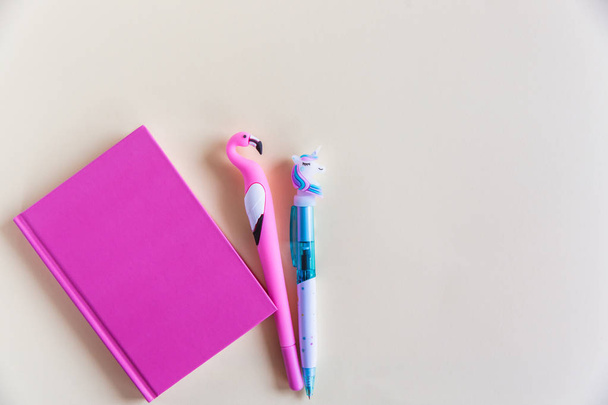 Caderno rosa para notas, unicórnio engraçado e canetas flamingo no fundo pastel amarelo. Deitado. Vista superior. Espaço de cópia
 - Foto, Imagem