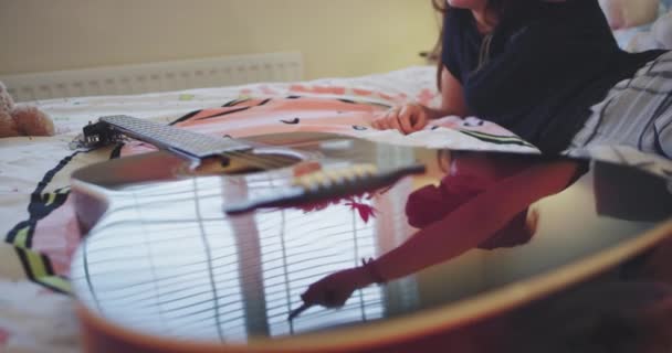 Detalhes de uma guitarra que reflete uma adolescente que usa óculos de realidade virtual em sua cama deitada no cobertor e carismática brincando com um VR vestindo um pijama. 4k
 - Filmagem, Vídeo