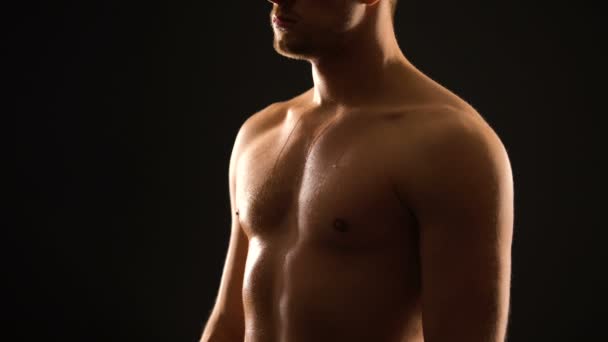 Masculine sweaty man standing against black background, athletic healthy body - Footage, Video