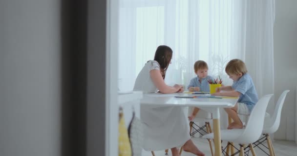 Äiti ja hänen kaksi poikaansa istuu keittiön pöydässä piirustus värillisiä kyniä perhe piirustus nurmikolla kesällä
. - Materiaali, video