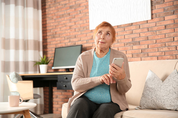 Elderly woman using smartphone on sofa in living room - Foto, Imagen