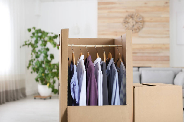 Cardboard wardrobe box with clothes on hangers in living room - Φωτογραφία, εικόνα