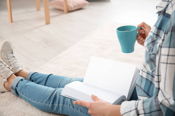 Hermosa mujer joven con taza de libro de lectura de café en el suelo en casa
 - Foto, Imagen