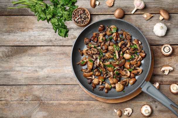 Frying pan of mushrooms on wooden background, flat lay with space for text - Fotó, kép