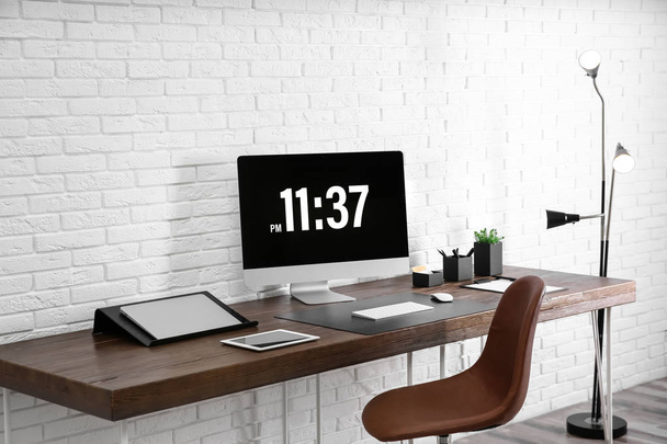 Modern workplace interior with computer and devices on table near brick wall - Фото, изображение
