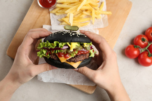 Woman holding black burger at served table, closeup - Photo, Image