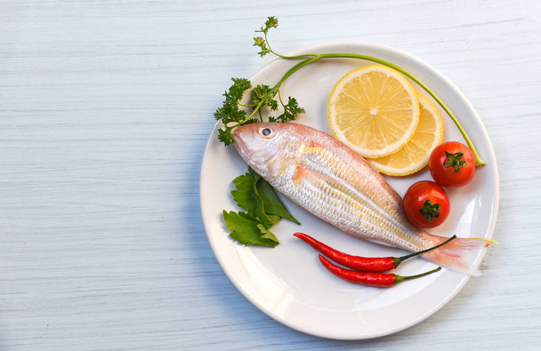 Piatto di pesce al limone prezzemolo peperoncino e pomodoro su piatto bianco
 - Foto, immagini