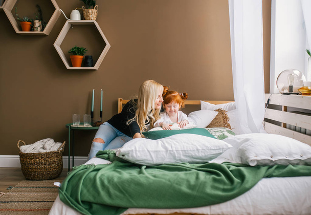 Yatakta oturan genç anne ve küçük Redhead kızı. - Fotoğraf, Görsel