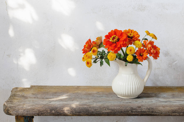 autumn flowers in pitcher on wooden bench - Photo, image