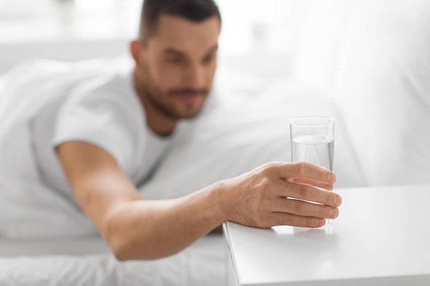 close up of man in bed reaching to glass of water  - Φωτογραφία, εικόνα