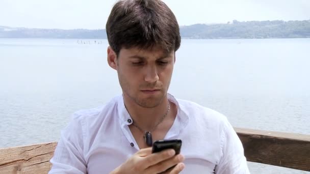 gutaussehender Geschäftsmann, der im Urlaub am See SMS schreibt - Filmmaterial, Video