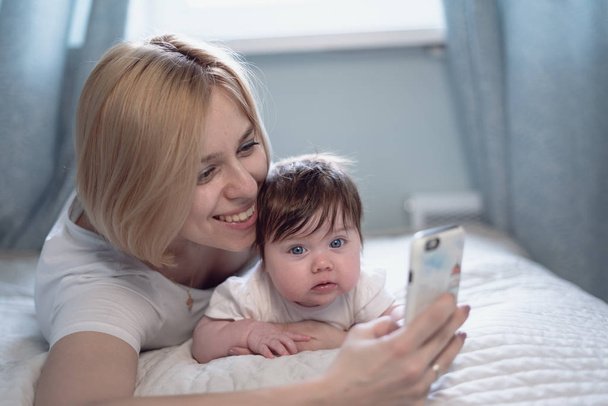 Young mother taking selfie with her cute baby on bed - Zdjęcie, obraz