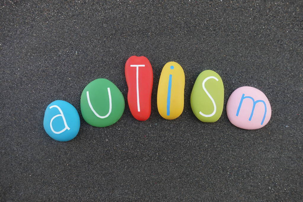 Autisme, autismespectrumstoornis, ziekte naam samengesteld met gekleurde stenen over zwart zand - Foto, afbeelding