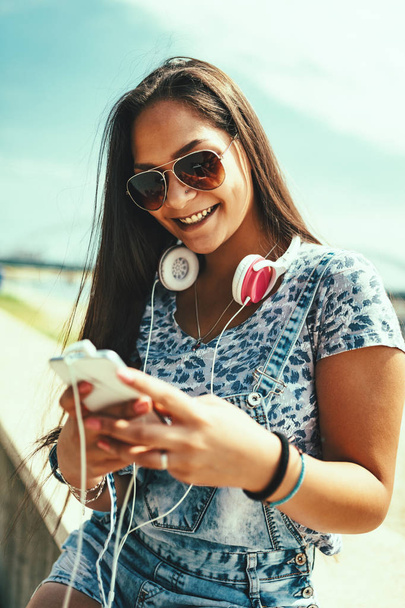 cheerful young woman listening music from smartphone on riverbank - 写真・画像