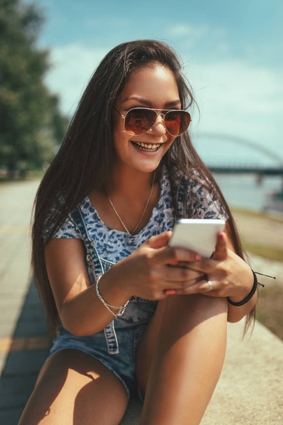 vidám, fiatal nő hallgat zenét a smartphone a folyóparton - Fotó, kép