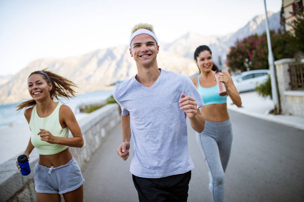 Outdoor portrait of group of friends running and jogging at seaside - Photo, image