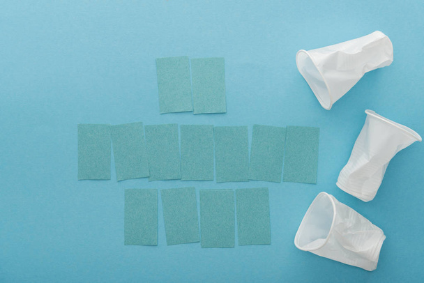 top view of white plastic cups and empty sticky notes with copy space on blue background  - Foto, Imagen