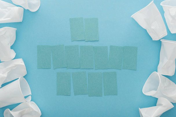 top view of white plastic cups and blank sticky notes with copy space on blue background  - Foto, Bild