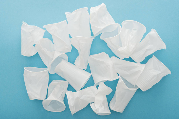 top view of white and crumpled plastic cups on blue background  - Фото, изображение