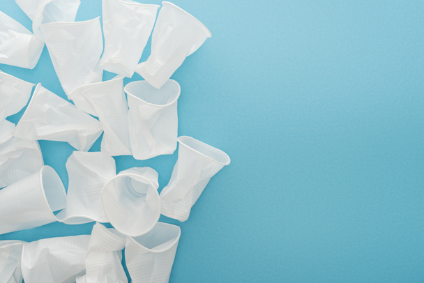 top view of white and crumpled plastic cups on blue background with copy space  - Foto, afbeelding