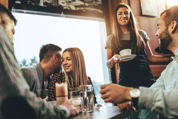  jonge serveerster serveren groep van jonge glimlachend vrienden in café - Foto, afbeelding