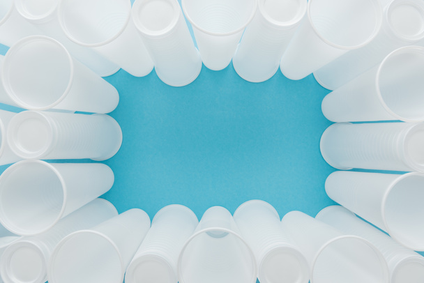 Draufsicht auf weiße Plastikbecher auf blauem Hintergrund mit Kopierraum  - Foto, Bild