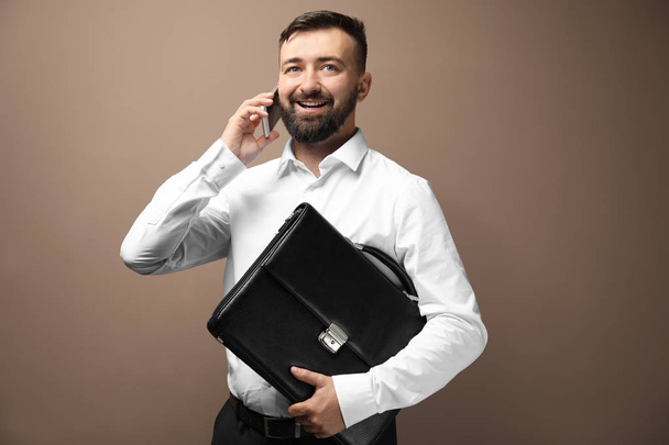 Businessman with bag speaking by phone on color background - Photo, image