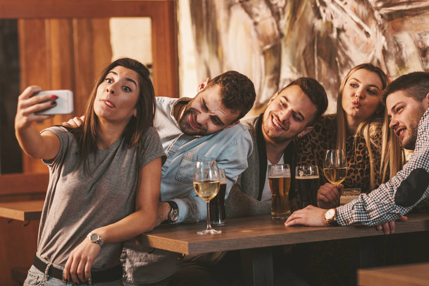 Молодая группа друзей делает смешные лица и делает селфи со смартфоном в кафе
 - Фото, изображение