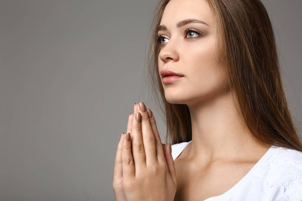Όμορφη νεαρή γυναίκα που προσεύχεται σε γκρίζο φόντο - Φωτογραφία, εικόνα