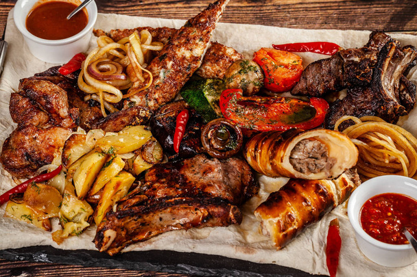 Concept of Georgian cuisine. Large meat board with shashlik, roasted meat, french fries, roast lamb and sauce. Serving dishes in a restaurant on a pita. Top view, copy space - Fotografie, Obrázek