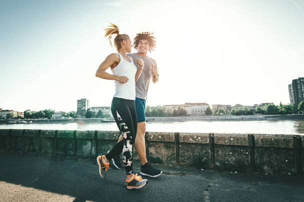 Young couple jogging outside by river at sunrise - Photo, Image