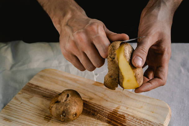 Şef patates temizler. Patates ile yemekler için. Siyah bir arka plan, menü, yemek, sağlıklı beslenme kavramı  - Fotoğraf, Görsel