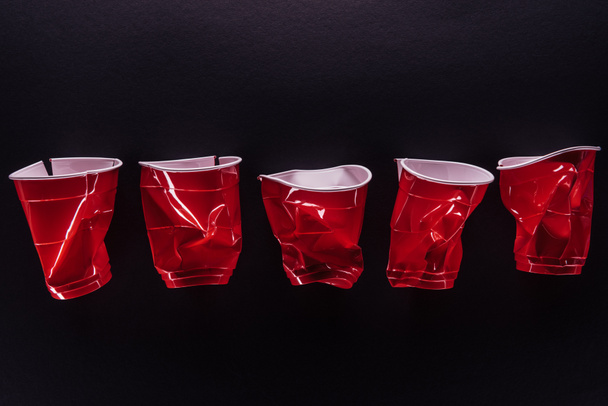 вид зверху яскраві і барвисті червоні пластикові чашки ізольовані на чорному
 - Фото, зображення