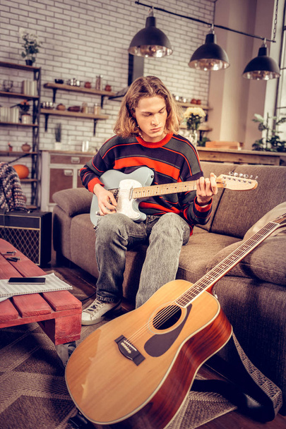 Student wearing jeans playing the guitar sitting on sofa - Valokuva, kuva